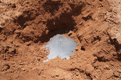 A hole in dirt revealing approximately 6 sq. in. of a geomembrane in which a very small hole has been found