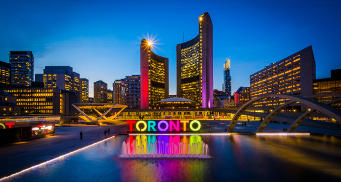 View of Nathan Phillips Square and Toronto Sign in downtown at night, in Toronto, Ontario by Jon Bilous via Shutterstock.